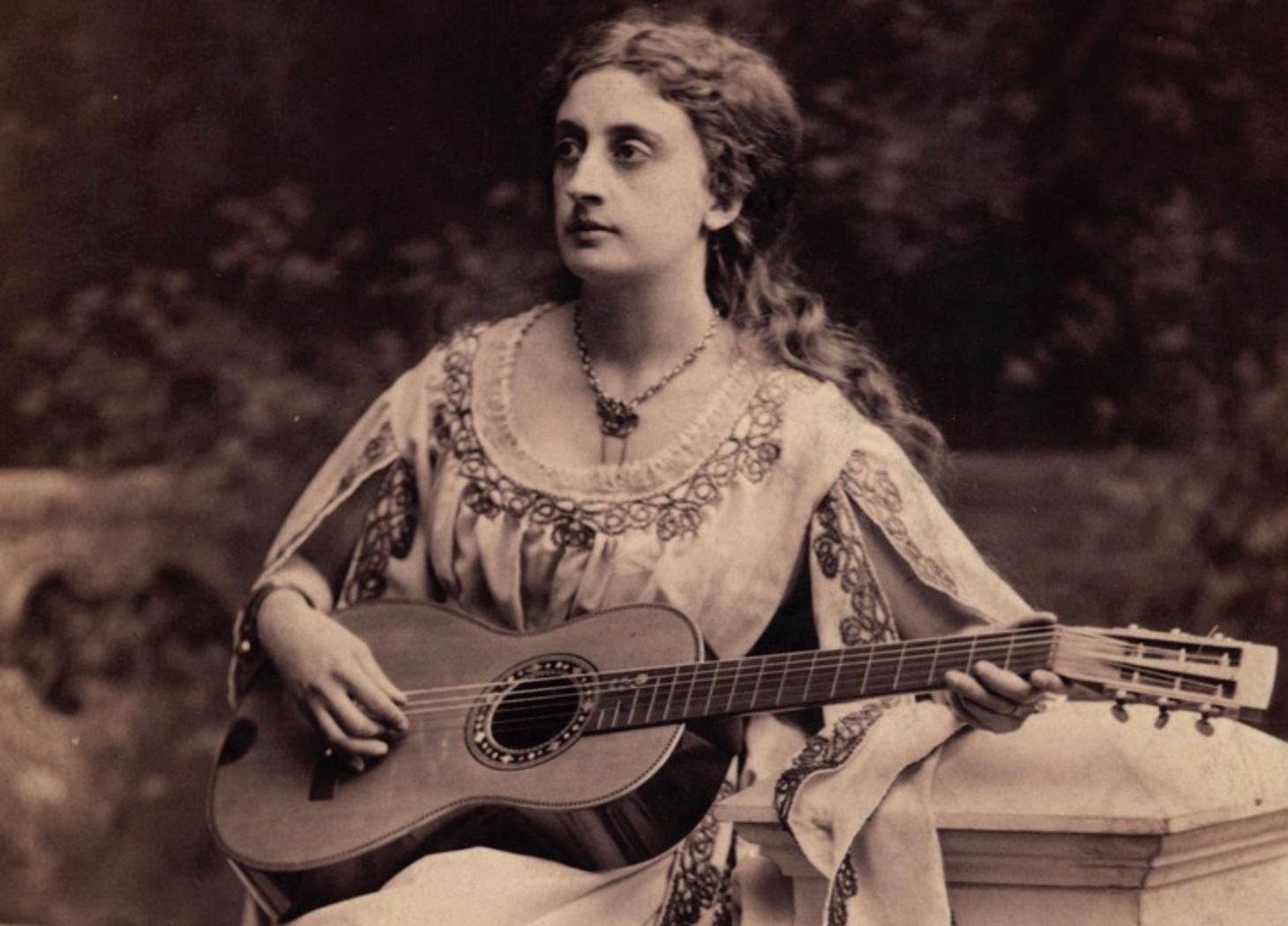 A sepia photo of a real cool woman with long, flowing hair playing acoustic guitar.